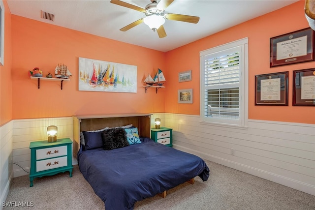 carpeted bedroom featuring a ceiling fan, wood walls, wainscoting, and visible vents