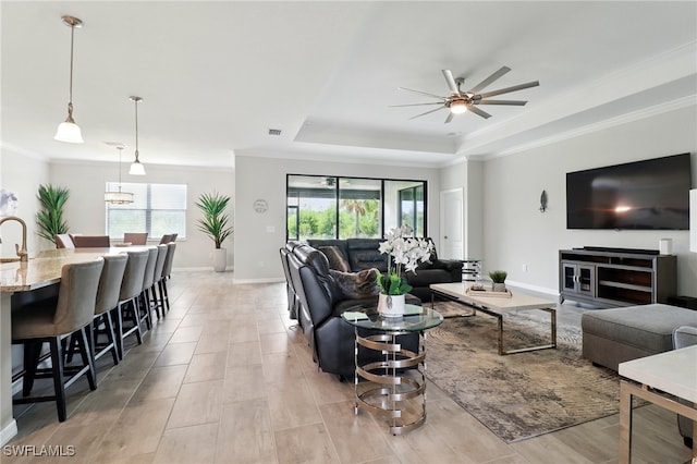 living room featuring a ceiling fan, a tray ceiling, visible vents, baseboards, and ornamental molding