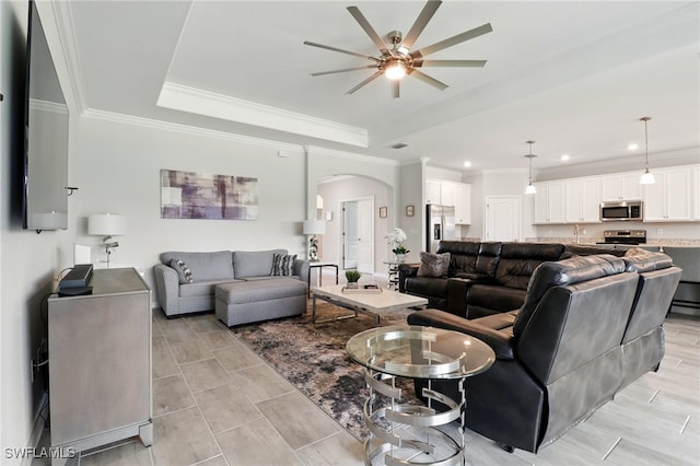 living area featuring arched walkways, a raised ceiling, ornamental molding, and a ceiling fan