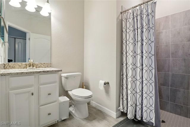 bathroom featuring vanity, toilet, baseboards, and tiled shower