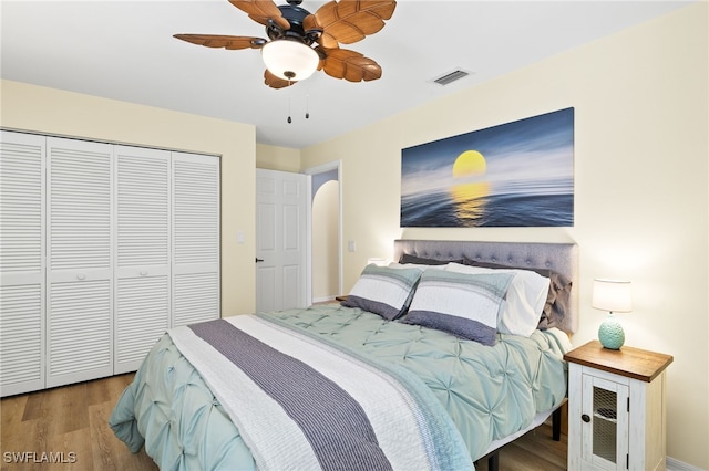 bedroom featuring ceiling fan, visible vents, wood finished floors, baseboards, and a closet