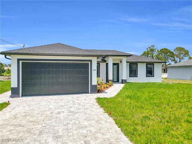 prairie-style house with an attached garage, decorative driveway, stucco siding, and a front yard