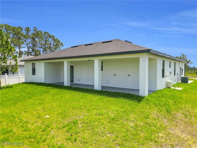 rear view of house with a lawn, central AC unit, fence, and stucco siding