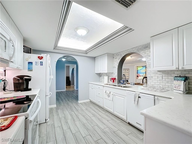 kitchen with a sink, light countertops, arched walkways, white appliances, and decorative backsplash