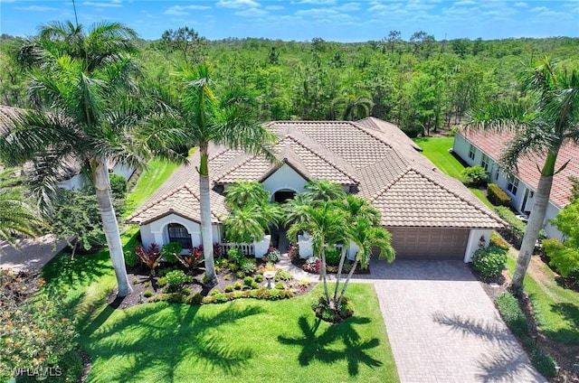 exterior space featuring a tiled roof, a garage, decorative driveway, a wooded view, and stucco siding