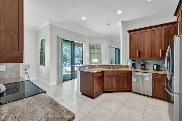 kitchen featuring stainless steel appliances, a sink, light stone countertops, a peninsula, and crown molding