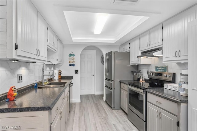 7666 Laurel Valley Rd, Fort Myers, FL 33967 - kitchen with stainless steel appliances, under cabinet range hood, a raised ceiling, dark countertops, and arched walkways