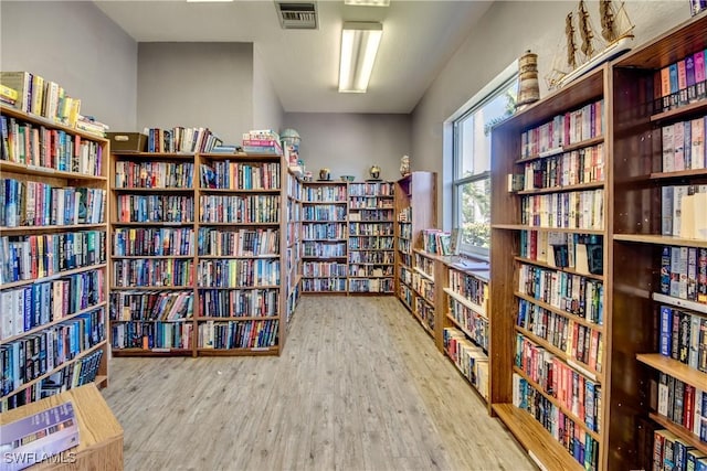 living area featuring visible vents, wall of books, and wood finished floors