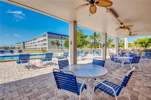 view of patio / terrace featuring outdoor dining space, fence, a ceiling fan, and a community pool
