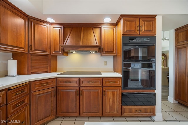 kitchen featuring a warming drawer, premium range hood, light countertops, light tile patterned floors, and black appliances