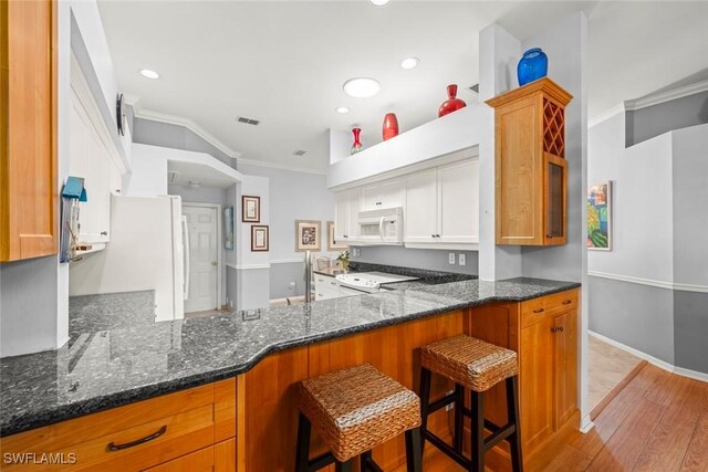 kitchen with white appliances, crown molding, dark stone counters, light wood finished floors, and white cabinetry