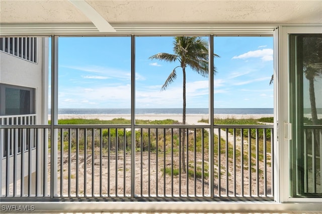unfurnished sunroom featuring a water view, beamed ceiling, a wealth of natural light, and a view of the beach