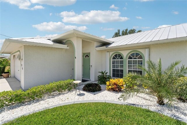 914 SW 3rd Ave, Cape Coral, FL 33991 - doorway to property with an attached garage, stucco siding, and metal roof