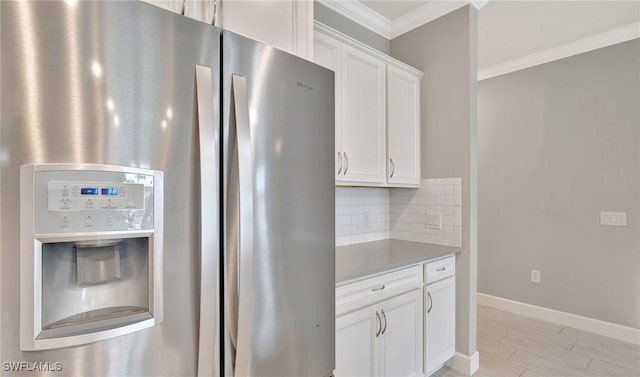 kitchen with ornamental molding, decorative backsplash, stainless steel fridge, light countertops, and white cabinetry