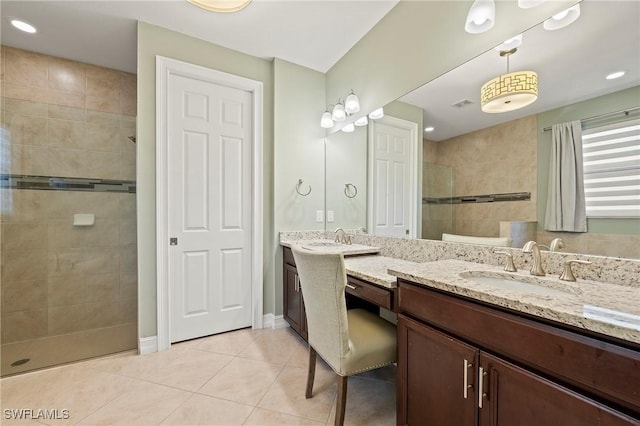 bathroom with tile patterned flooring, visible vents, vanity, baseboards, and a tile shower