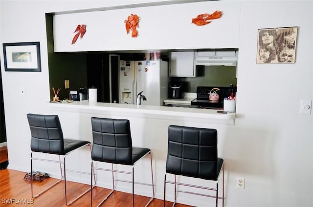 6053 Timberwood Cir Unit 233, Fort Myers, FL 33908 - kitchen featuring a kitchen breakfast bar, white refrigerator with ice dispenser, black range with electric stovetop, wood finished floors, and under cabinet range hood