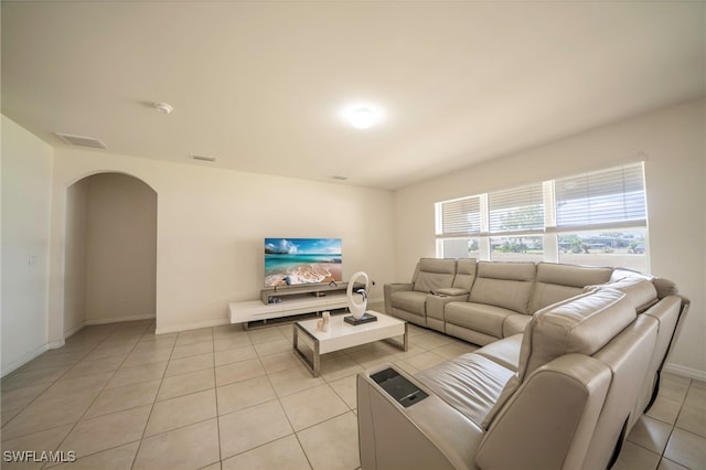 living room featuring light tile patterned floors, arched walkways, baseboards, and visible vents
