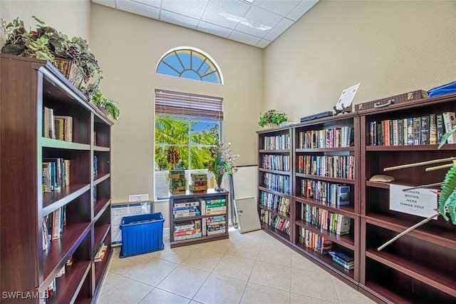 living area featuring wall of books, a drop ceiling, and tile patterned flooring