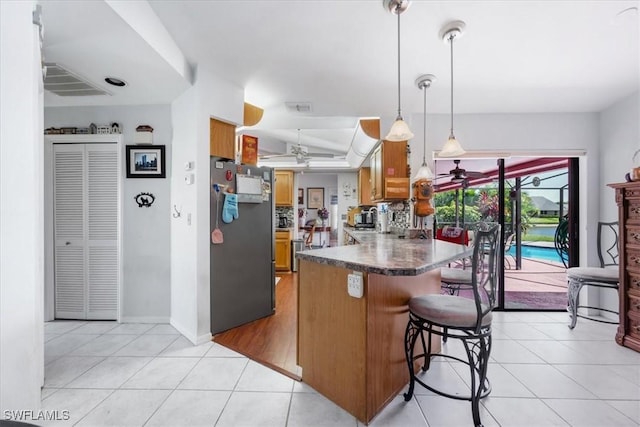 kitchen with brown cabinetry, freestanding refrigerator, a peninsula, a ceiling fan, and light tile patterned floors