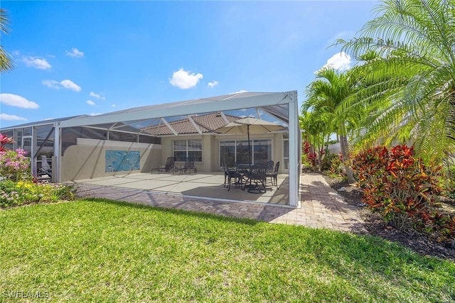 rear view of house with a patio, stucco siding, a yard, and glass enclosure