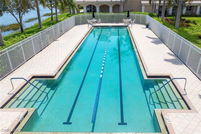 community pool featuring fence, a water view, and a patio area