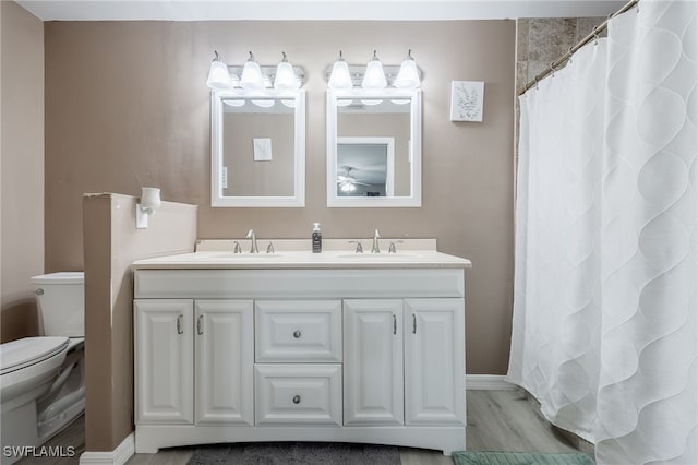 full bathroom with toilet, ceiling fan, double vanity, baseboards, and wood finished floors