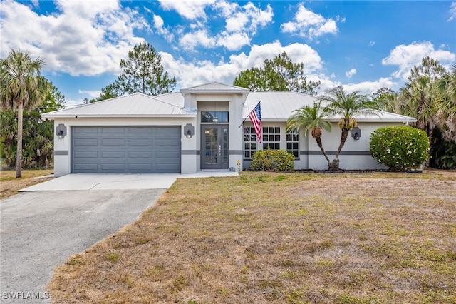 view of front of home with asphalt driveway, a garage, a front lawn, metal roof, and stucco siding