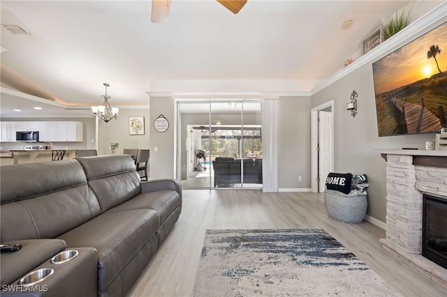 living room with a ceiling fan, light wood-style floors, a chandelier, a stone fireplace, and ornamental molding