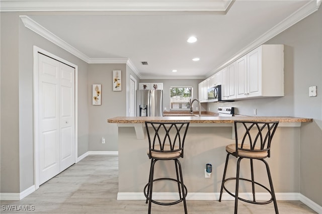 kitchen with stainless steel appliances, a peninsula, white cabinets, ornamental molding, and a kitchen breakfast bar