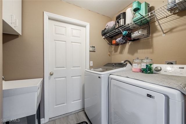 laundry area with independent washer and dryer, cabinet space, and light wood-style flooring