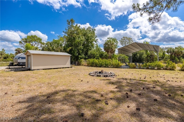 view of green lawn with a detached carport, an outbuilding, and a fire pit