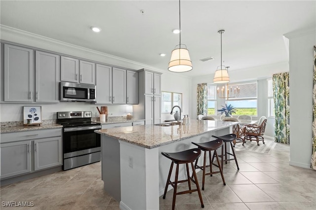 kitchen with an island with sink, a kitchen breakfast bar, a sink, appliances with stainless steel finishes, and gray cabinetry
