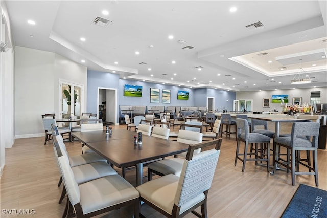 dining area with a tray ceiling, visible vents, and light wood-type flooring