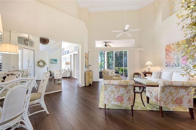 living room featuring crown molding, dark wood-style flooring, baseboards, ceiling fan, and a high ceiling