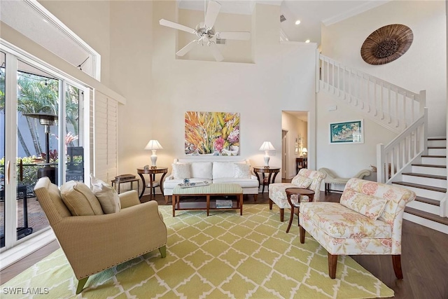 living area with stairway, a high ceiling, a ceiling fan, and wood finished floors