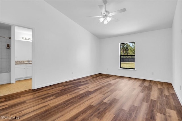 spare room featuring vaulted ceiling, wood finished floors, baseboards, and ceiling fan