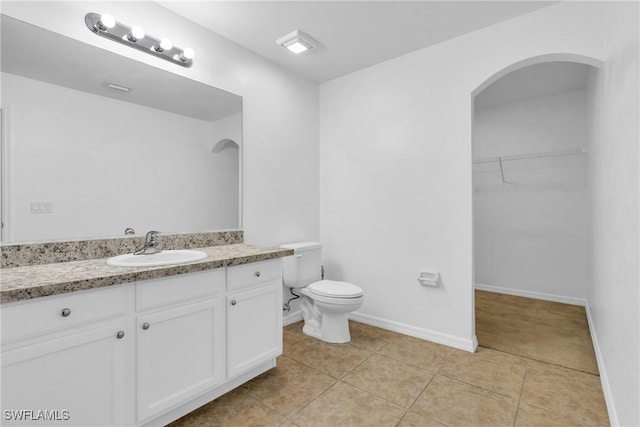 bathroom with toilet, a walk in closet, baseboards, tile patterned flooring, and vanity