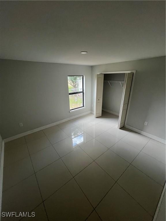 unfurnished bedroom with light tile patterned flooring, baseboards, and a closet