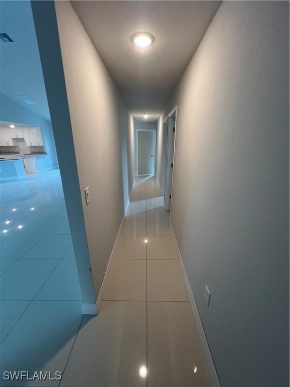 corridor featuring baseboards, light tile patterned flooring, and visible vents