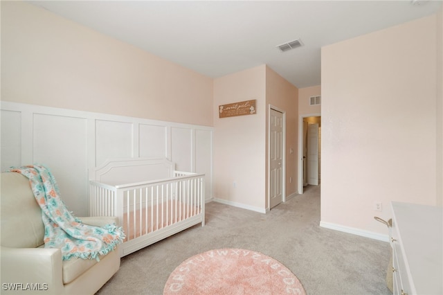 bedroom featuring light colored carpet, visible vents, a decorative wall, and wainscoting