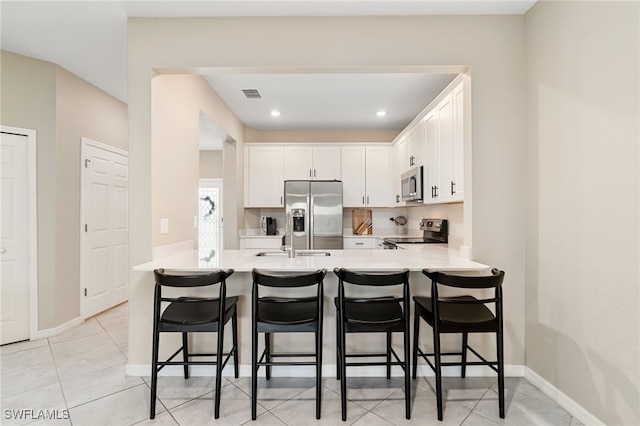 kitchen with a peninsula, a breakfast bar, stainless steel appliances, white cabinetry, and light countertops