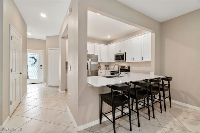 kitchen featuring a peninsula, light tile patterned flooring, a kitchen breakfast bar, light countertops, and appliances with stainless steel finishes