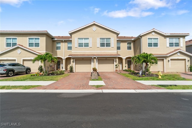 townhome / multi-family property with an attached garage, stucco siding, a tiled roof, and driveway