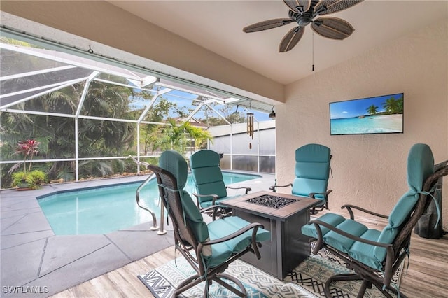 pool featuring glass enclosure, ceiling fan, a patio area, and an outdoor fire pit
