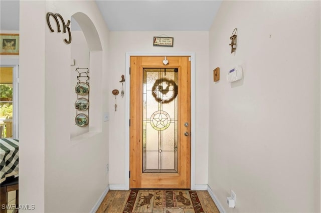 entryway featuring wood finished floors, baseboards, and arched walkways