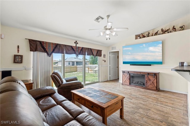living area featuring light wood finished floors, visible vents, ceiling fan, and a glass covered fireplace