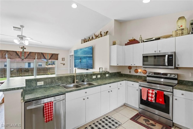 kitchen with lofted ceiling, a sink, a peninsula, dark countertops, and appliances with stainless steel finishes
