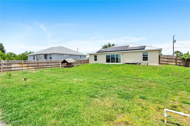 back of property featuring a yard, a fenced backyard, and roof mounted solar panels