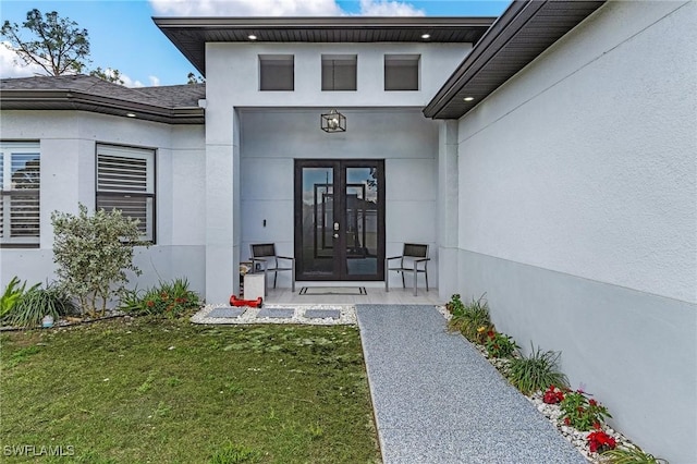 property entrance with stucco siding, a yard, and french doors