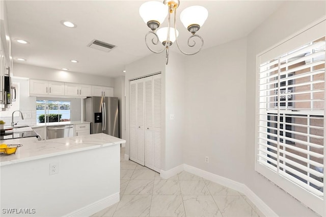 2524 Sailors Way Unit 118, Naples, FL 34109 - kitchen with a sink, light stone counters, an inviting chandelier, stainless steel appliances, and white cabinetry